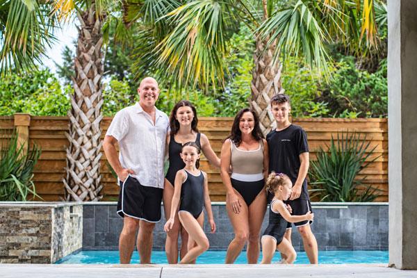 Family in matching bathing suits by a pool with palm trees in the background.